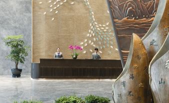 The lobby features a large stone wall with an artistic design, serving as a backdrop to the front desk at Grand Barony Qingdao Airport Hotel