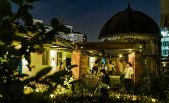 A group of people is standing outside at night near the bar and restaurant, while others are sitting on benches at POSHPACKER Local Tea Hostel