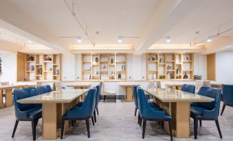 In the middle of the room, there are tables and chairs, as well as an open bookshelf alongside them at Byland Star Hotel (Yiwu International Trade City)