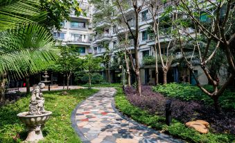 In front of the apartment building, there is a courtyard adorned with trees and plants at Guangzhou Feiyang Apartment