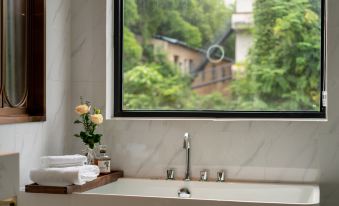 The bathroom, adorned in white linen, features a large window and a sink adjacent to the bathtub at Foshan Lanshan Hotel (Shunde Qinghuiyuan)