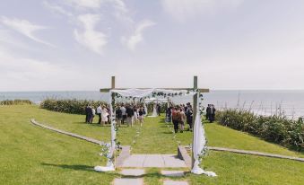 a wedding ceremony taking place on a grassy field near a body of water , with a group of people standing beneath a white arch at Castaways Resort