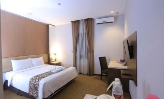 a hotel room with a bed , desk , and tv , along with some items on the desk at Tjokro Hotel Klaten