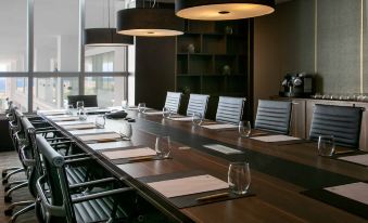 a long wooden table is set with wine glasses , napkins , and place mats in a room with large windows at NissiBlu Beach Resort