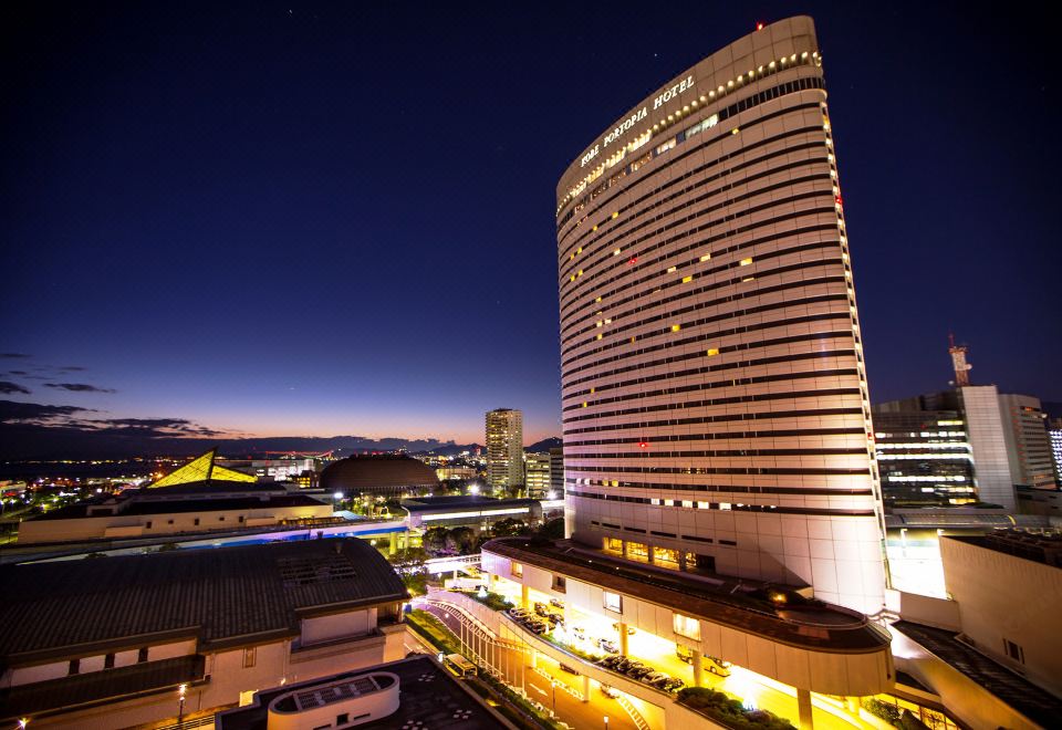 a tall hotel building surrounded by a city , with the sun setting in the background at Kobe Portopia Hotel