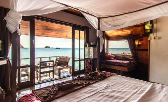 a bedroom with a bed , chairs , and a view of the ocean through large windows at Taatoh Seaview Resort