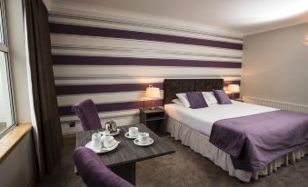 a hotel room with a purple and white striped bed , two chairs , a dining table , and a television at Brandon House Hotel