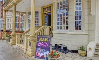 "a storefront with a sign that says "" bar open "" and a flower arrangement on the steps" at Empire Hotel
