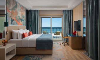 a modern hotel room with a large window offering a view of the ocean , featuring a bed , desk , and tv at Rixos Water World Aktau