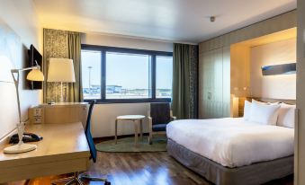 a modern hotel room with a large window , wooden floors , and a white bed , along with other furniture at Hilton Helsinki Airport