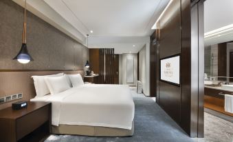 A modern bedroom with a large bed and TV in the middle, alongside an open at Grand Barony Qingdao Airport Hotel