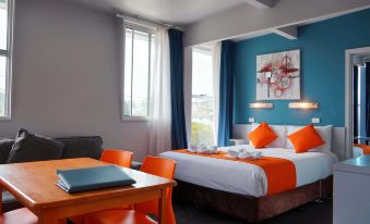 a hotel room with a blue and orange theme , featuring a bed , a dining table , and a chair at Waterfront Lodge Motel