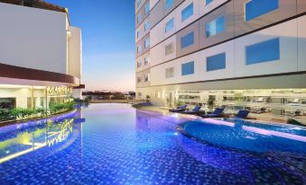 a modern building with a large swimming pool and sun loungers , set against a clear blue sky at Aston Kupang Hotel & Convention Center