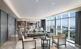 The ground floor of the hotel features a spacious living room with large windows and modern furniture, including couches at Grand Barony Qingdao Airport Hotel