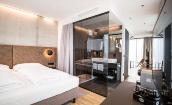 a modern bedroom with a large bed and a glass partition separating the bedroom from the bathroom at Arte Hotel Salzburg