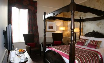 a bedroom with a four - poster bed , a chair , and a dining table in the room at Coulsdon Manor Hotel and Golf Club