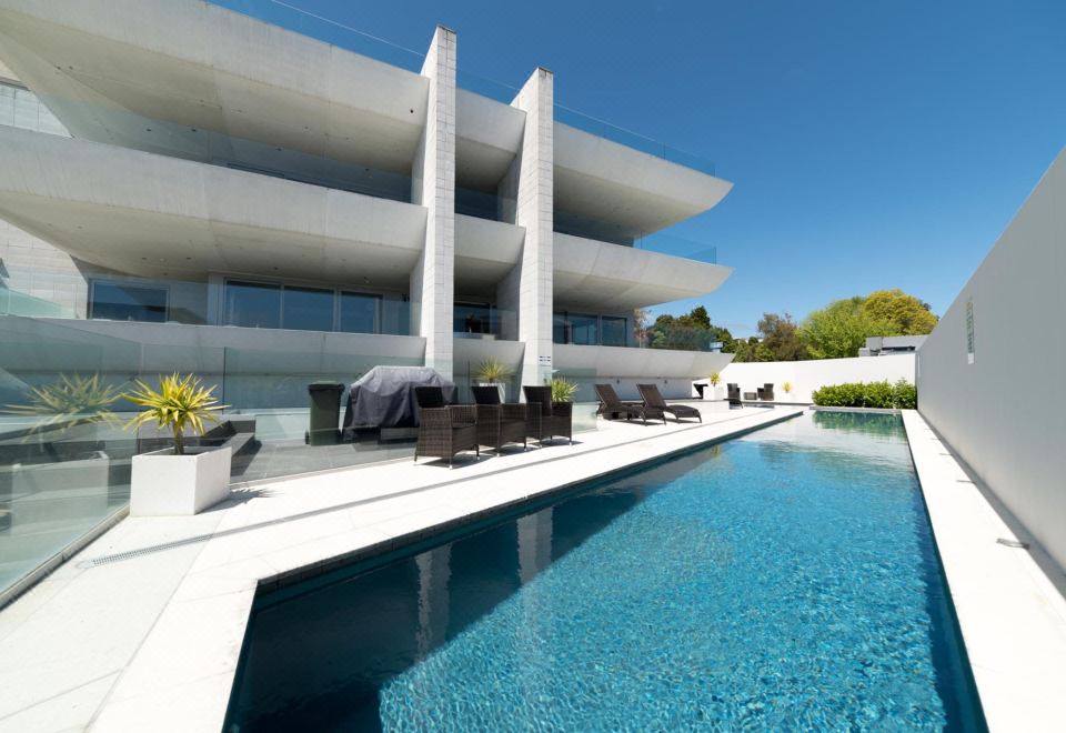 a modern , white building with a large swimming pool and lounge chairs in front of it at Sacred Waters Taupo