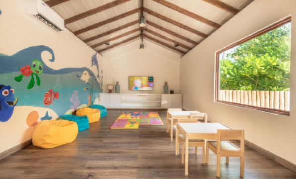 a cozy living room with a wooden floor , a large flat - screen tv mounted on the wall , and several chairs arranged around a dining table at Fushifaru Maldives