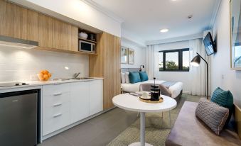 a modern kitchen and living room area with a white table , blue pillows , and wooden cabinets at Quest Cannon Hill