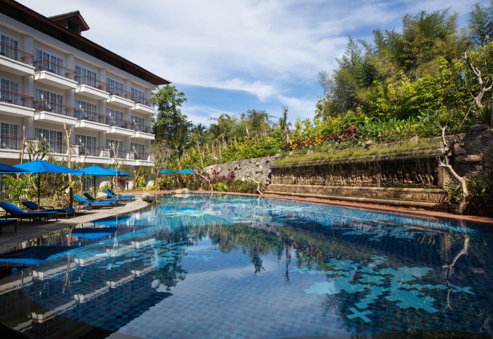 a large swimming pool is surrounded by a resort with multiple buildings and palm trees at Plataran Heritage Borobudur Hotel