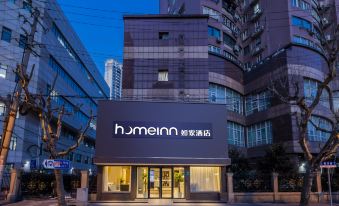 At night, a hotel's front entrance is illuminated by a sign above it, surrounded by other buildings at Homeinn · neo (Shanghai Nanjing Road Pedestrian Street Huanghe Road)