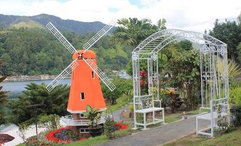 a windmill in a park , surrounded by trees and flowers , with a white archway and a bench nearby at Khas Parapat