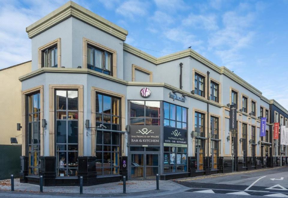 a modern building with a white facade and a large window , located on a street corner at The Prince of Wales Hotel