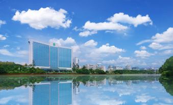 a large building with a blue glass facade is reflected in the water , surrounded by greenery and clouds at Lakeside Hotel