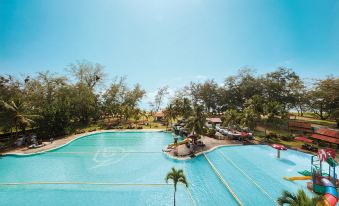 a large outdoor swimming pool surrounded by palm trees , with a view of the ocean in the background at Resorts World Kijal