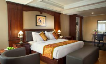 a large bed with white linens and a gold throw is in the center of a room with wooden furniture at The Rich Jogja Hotel