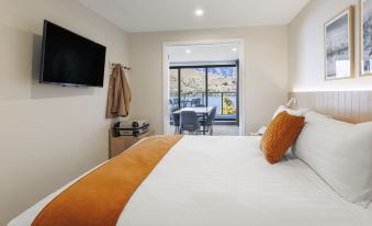 a cozy bedroom with a large bed and a tv mounted on the wall , overlooking a balcony with a table and chairs at Oaks Queenstown Shores Resort