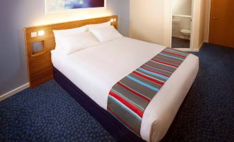 a neatly made bed with white sheets and a striped blanket is shown in a hotel room at Travelodge Porthmadog
