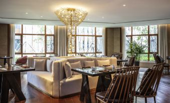 a modern living room with a large window , wooden floor , and comfortable furniture under a crystal chandelier at Pullman Changbaishan Resort