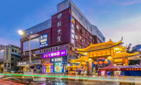 In a city at night, there is a street lined with buildings and people, including an Asian individual at Seven Orange Hotel (Guangzhou Railway Station)