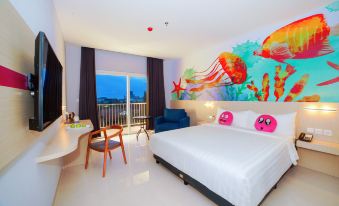 a hotel room with a large bed , colorful artwork on the wall , and a view of the ocean at favehotel Bitung