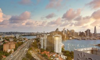 a cityscape with a large building in the foreground and boats on the water in the background at Meriton Suites North Sydney