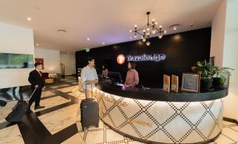 a reception desk in a hotel lobby with two people standing behind it , one of them holding a suitcase at Travelodge Ipoh