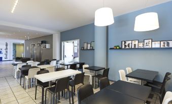 a dining area with several tables and chairs , some of which are covered in black tablecloths at B&B Hotel Bologna