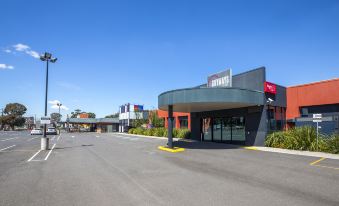 a modern building with a curved entrance and red accents is situated on a street at Nightcap at Skyways Hotel