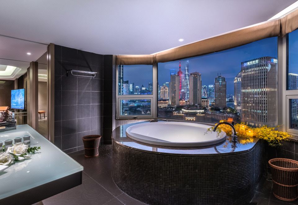 The bathroom features large windows with a city view and an oval-shaped bathtub at Elegant Hotel Shanghai Bund