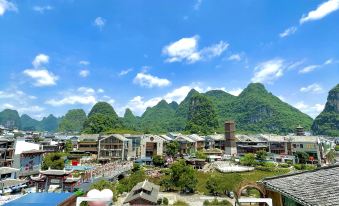 The hotel offers a picturesque view from its rooftop, showcasing mountains, a blue sky, and white clouds in the background at Zhenmei Resort Chain Hotel(Yangshuo West Street AiYuan Store)