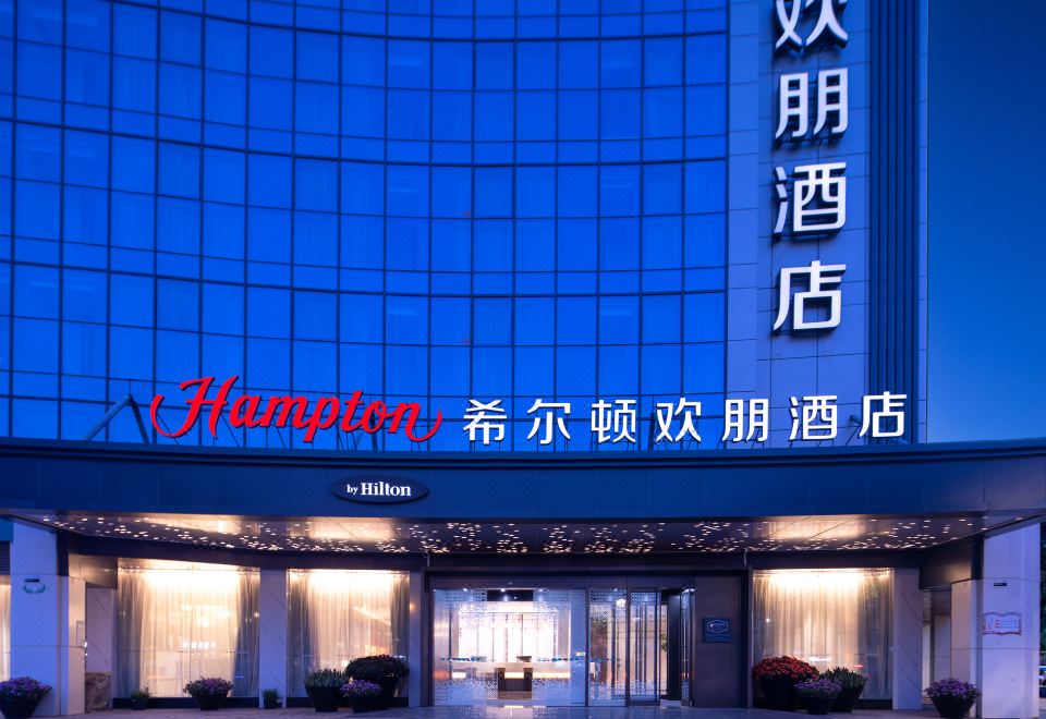 At night, the front entrance of a hotel displays its sign in both Chinese and Japanese languages at Hampton by Hilton Yiwu International Trade Market