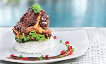 a plate of food on a dining table , consisting of rice , meat , and vegetables , placed next to a swimming pool at Favehotel Cimanuk Garut