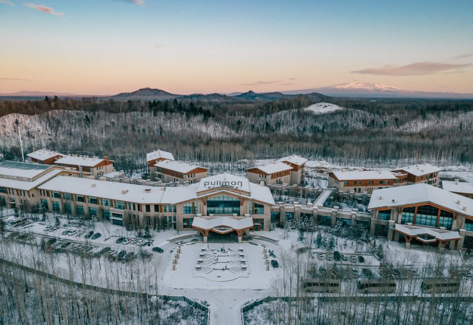 aerial view of a large resort with snow - covered mountains in the background , surrounded by trees at Pullman Changbaishan Resort