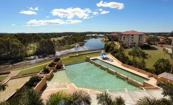 a large swimming pool with a house and trees in the background , surrounded by grass and water at Pelican Waters Resort