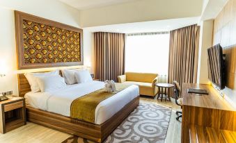 a large bed with a white and gold comforter is in the middle of a room with a couch , chair , and desk at Horison Ultima Bandung