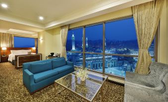 a modern living room with blue couches , a glass coffee table , and large windows offering a view of the city at night at Hilton Suites Makkah
