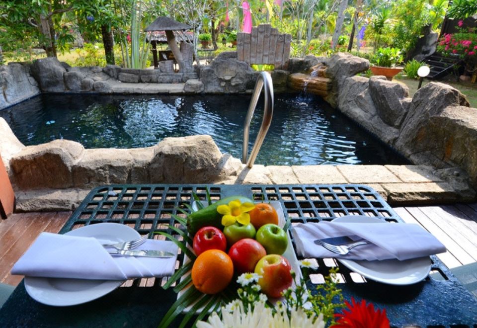 a table set with plates , napkins , and a vase of fruit near a pool surrounded by rocks at Lavilla by Holiday Villa Cherating