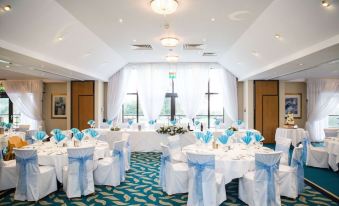 a wedding reception with white tablecloths , blue chairs , and flowers is set up in a large room with a high ceiling at Dale Hill Hotel