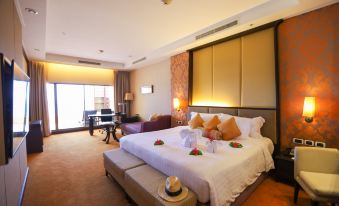 a large bed with white sheets and orange pillows is in a room with a couch and sliding glass doors at Dusit Thani Pattaya